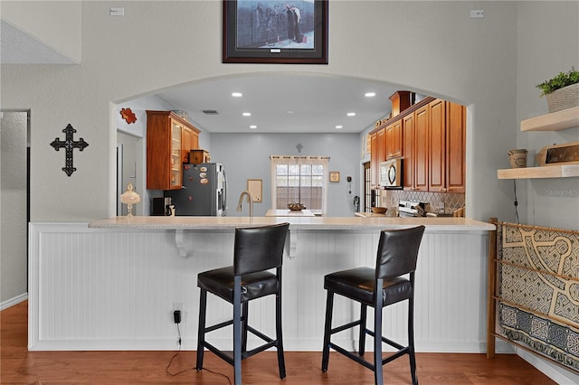 kitchen featuring backsplash, a kitchen breakfast bar, appliances with stainless steel finishes, light hardwood / wood-style floors, and kitchen peninsula