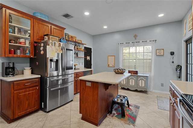 kitchen featuring light tile patterned floors, a kitchen breakfast bar, stainless steel fridge, a kitchen island, and range