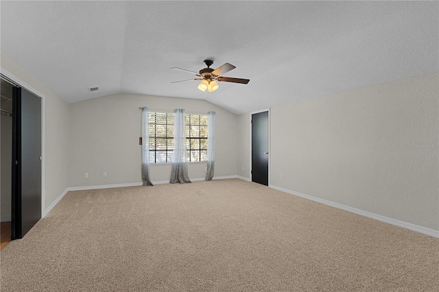 carpeted empty room featuring a textured ceiling, ceiling fan, and vaulted ceiling