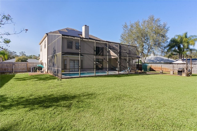 rear view of house featuring a lawn, glass enclosure, a fenced in pool, and solar panels