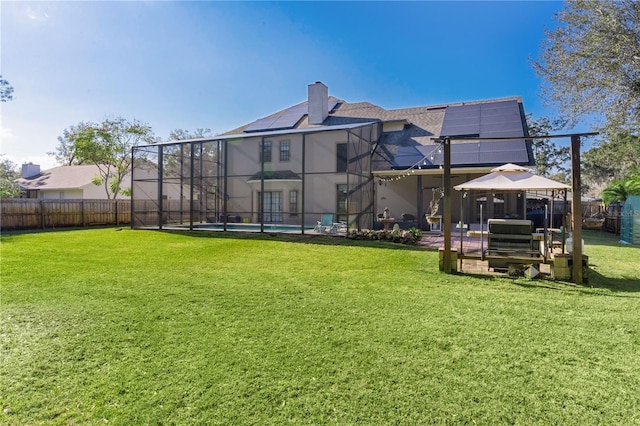 rear view of house featuring a lawn, solar panels, glass enclosure, a swimming pool, and a gazebo