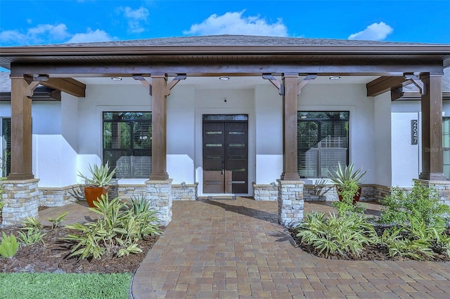 property entrance with stucco siding, stone siding, covered porch, and a shingled roof