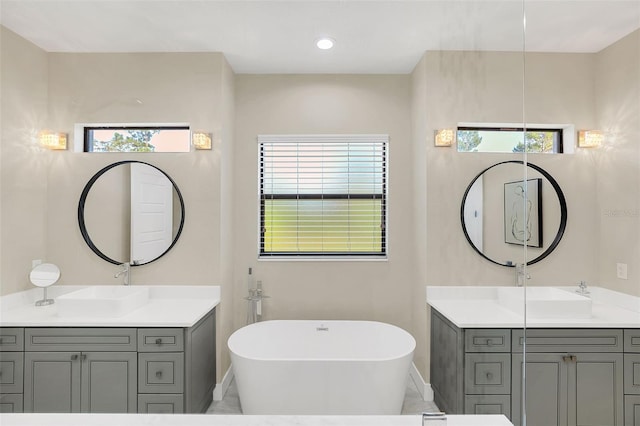 bathroom featuring a sink, a freestanding bath, two vanities, and recessed lighting