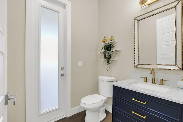 bathroom with toilet, vanity, baseboards, and wood finished floors