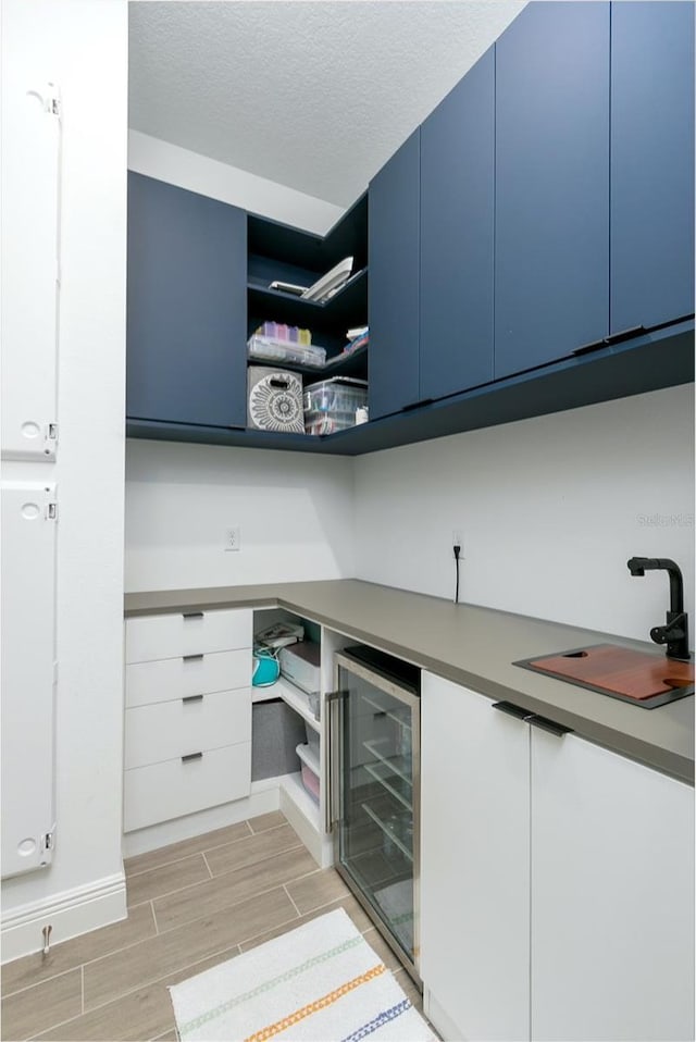 kitchen featuring blue cabinetry, white cabinetry, sink, wine cooler, and a textured ceiling