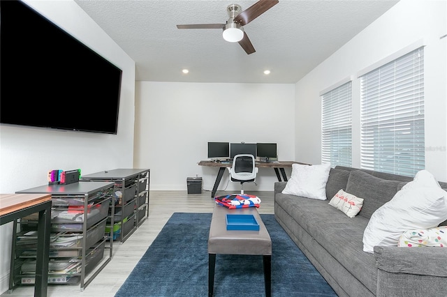 living room with a textured ceiling, light wood-type flooring, and ceiling fan