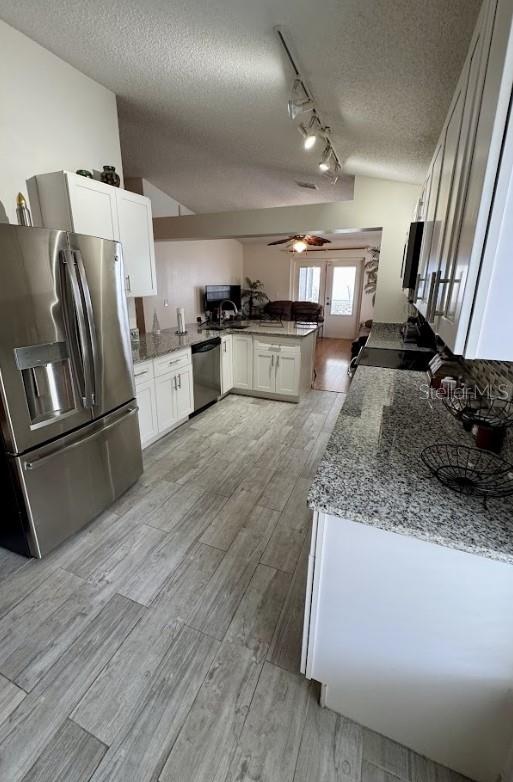 kitchen featuring rail lighting, white cabinets, kitchen peninsula, stainless steel appliances, and a textured ceiling