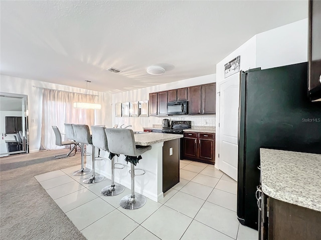 kitchen featuring a breakfast bar area, a center island, hanging light fixtures, light tile patterned floors, and black appliances