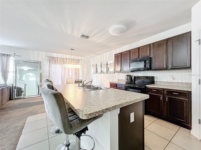 kitchen with a breakfast bar, pendant lighting, sink, black appliances, and a center island with sink