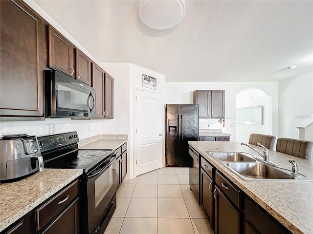 kitchen with sink, light tile patterned floors, backsplash, dark brown cabinets, and black appliances