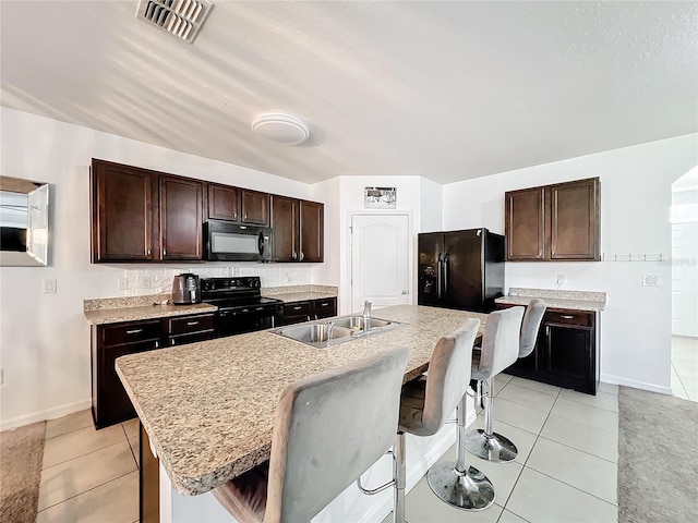 kitchen featuring dark brown cabinetry, sink, a breakfast bar area, a kitchen island with sink, and black appliances