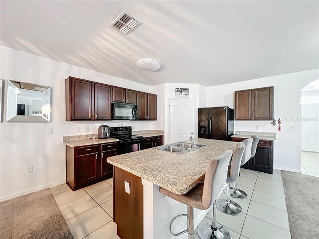 kitchen featuring sink, light tile patterned floors, a breakfast bar area, black appliances, and an island with sink