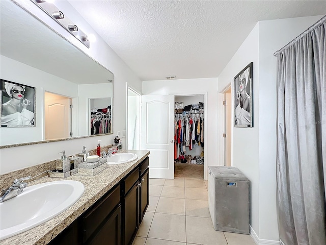6163 Forest Ridge Way, Winter Haven, FL 33881 - bathroom featuring a walk in closet, double vanity, tile patterned flooring, a textured ceiling, and baseboards