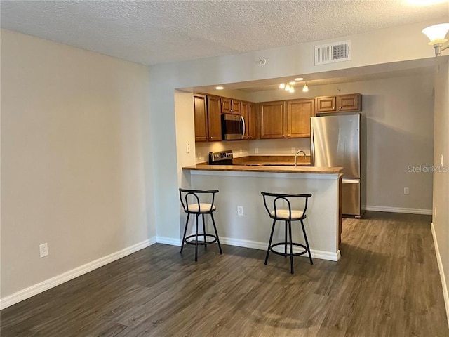 kitchen with kitchen peninsula, dark hardwood / wood-style flooring, stainless steel appliances, and a breakfast bar area