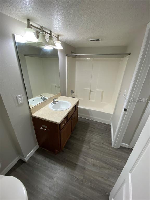 full bathroom featuring toilet, hardwood / wood-style floors, a textured ceiling, tub / shower combination, and vanity