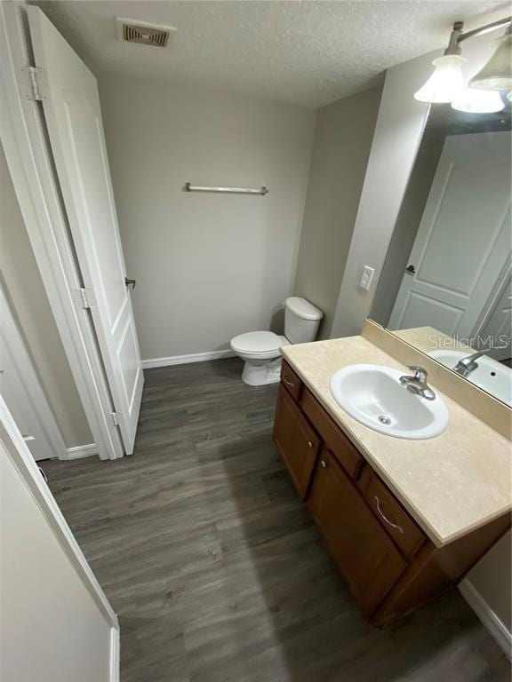 bathroom with toilet, vanity, a textured ceiling, and hardwood / wood-style floors