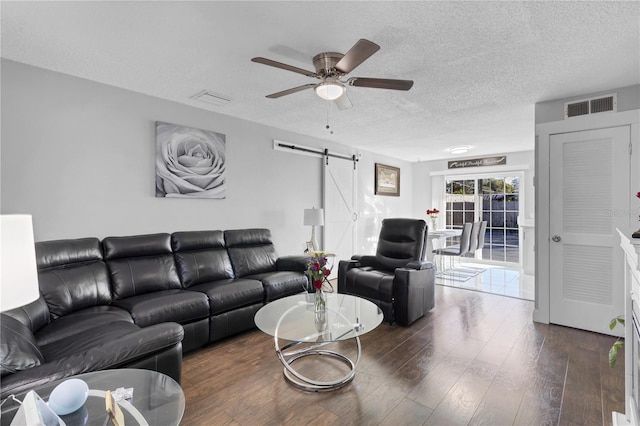 living room with ceiling fan, a barn door, dark hardwood / wood-style flooring, and a textured ceiling