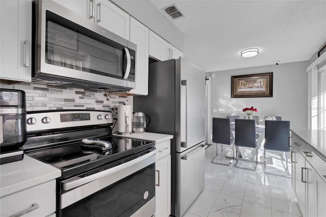 kitchen featuring a textured ceiling, tasteful backsplash, light stone counters, white cabinetry, and stainless steel appliances