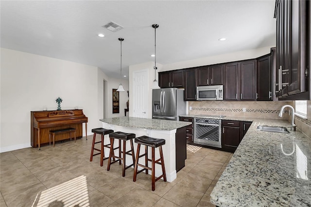 kitchen with pendant lighting, a center island, sink, light stone counters, and stainless steel appliances