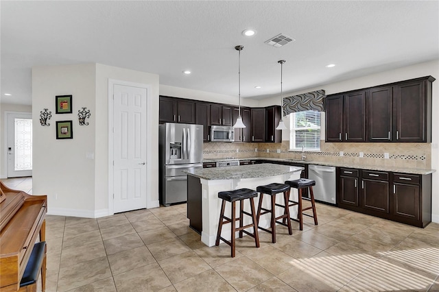 kitchen with a center island, hanging light fixtures, a kitchen breakfast bar, decorative backsplash, and appliances with stainless steel finishes