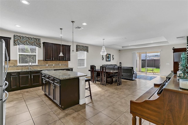 kitchen with pendant lighting, a kitchen island, a raised ceiling, and light tile patterned flooring