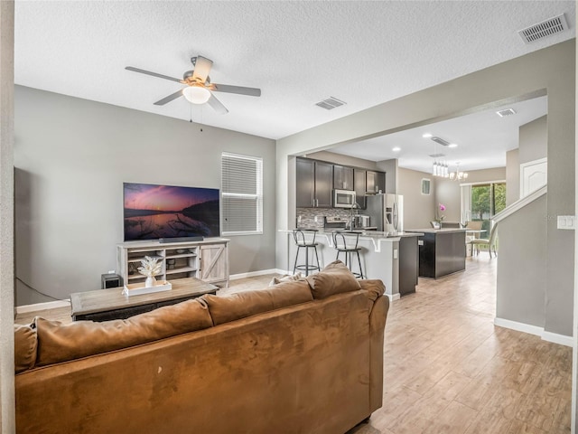 living room featuring ceiling fan with notable chandelier, a textured ceiling, and light hardwood / wood-style flooring