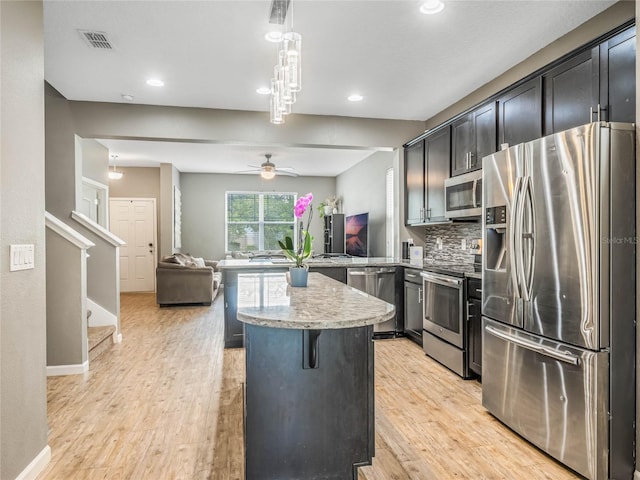 kitchen featuring pendant lighting, a breakfast bar, decorative backsplash, ceiling fan, and appliances with stainless steel finishes