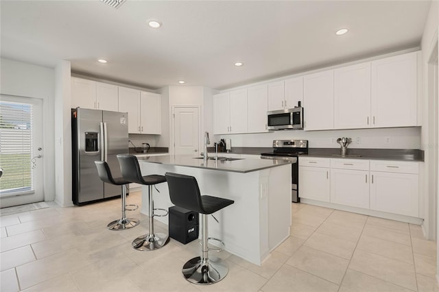 kitchen featuring a breakfast bar, a center island with sink, sink, white cabinetry, and stainless steel appliances