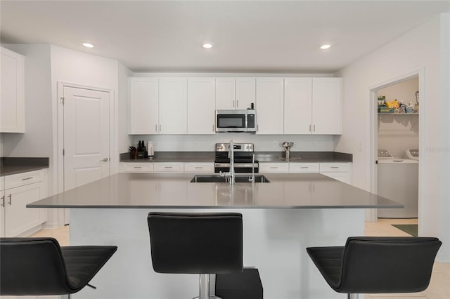 kitchen featuring stainless steel appliances, washer and clothes dryer, sink, white cabinetry, and a breakfast bar area