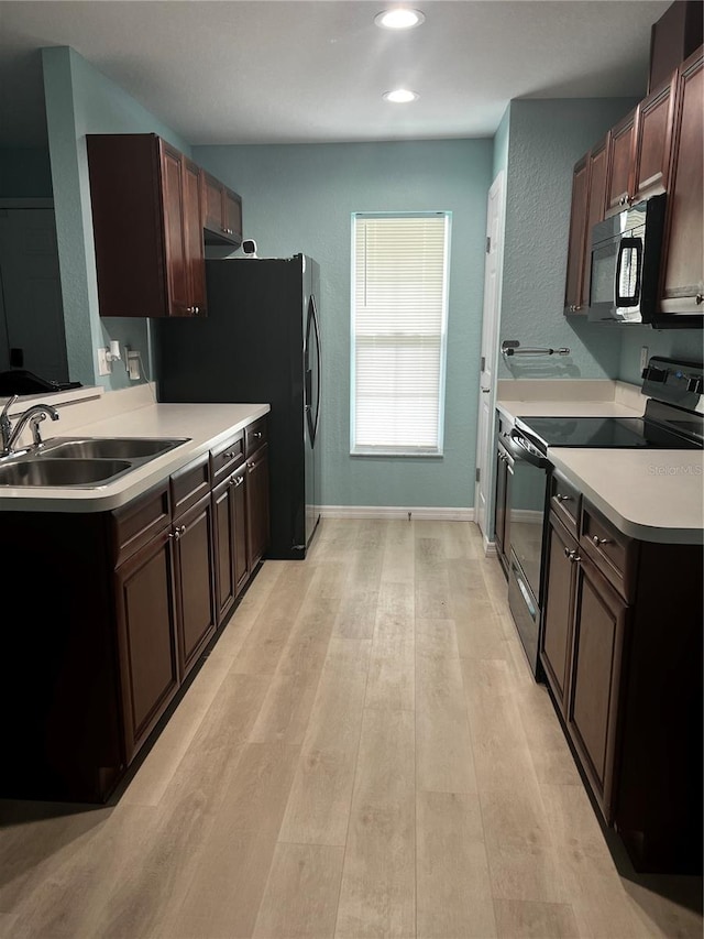 kitchen with sink, light hardwood / wood-style floors, dark brown cabinetry, and black appliances