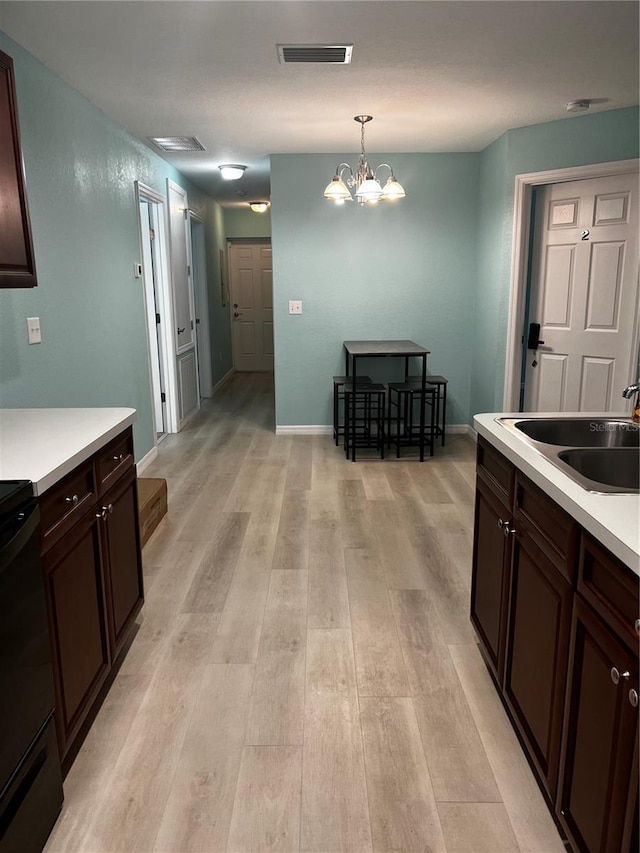 kitchen with dark brown cabinetry, sink, a notable chandelier, light hardwood / wood-style floors, and hanging light fixtures