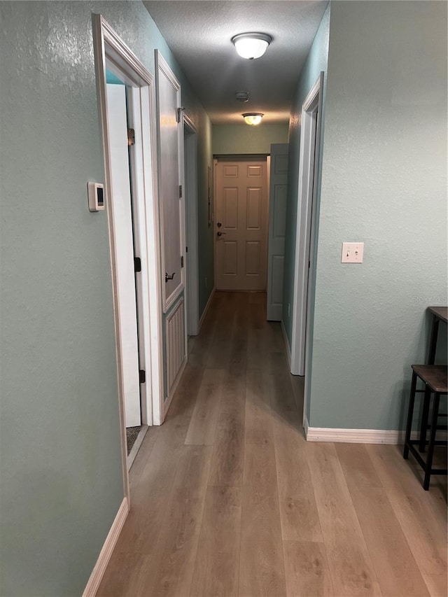 corridor with a textured ceiling and light wood-type flooring