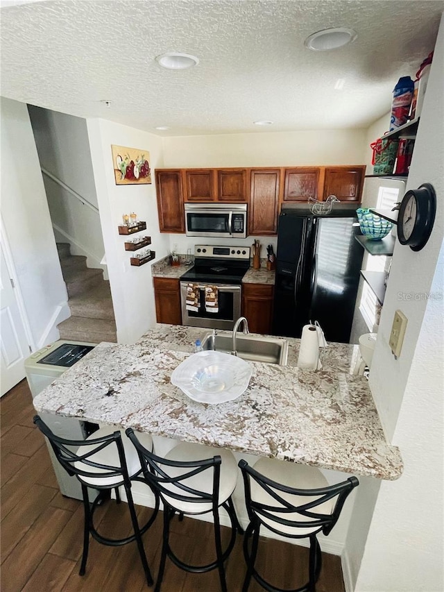 kitchen featuring sink, dark hardwood / wood-style floors, a textured ceiling, a kitchen bar, and appliances with stainless steel finishes