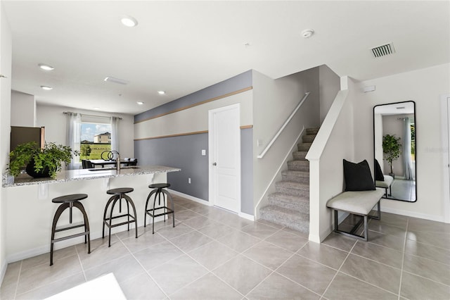 kitchen with a breakfast bar, sink, light stone countertops, light tile patterned floors, and kitchen peninsula