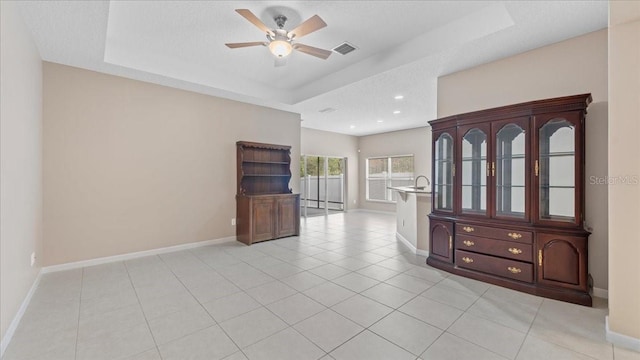 interior space with a raised ceiling, a textured ceiling, and ceiling fan