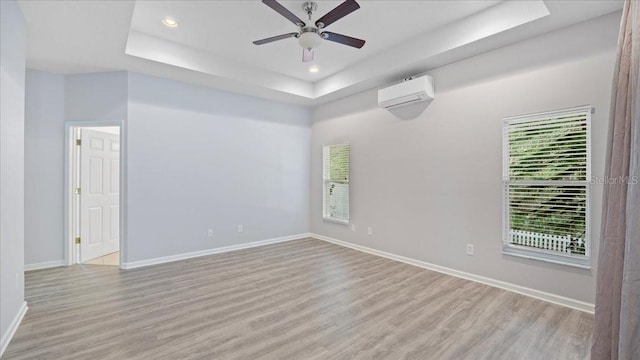 unfurnished room with ceiling fan, an AC wall unit, light wood-type flooring, and a tray ceiling