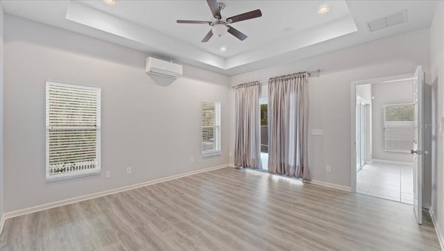 spare room featuring a raised ceiling, a wall mounted AC, ceiling fan, and light hardwood / wood-style flooring