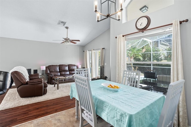 tiled dining room with high vaulted ceiling and ceiling fan with notable chandelier