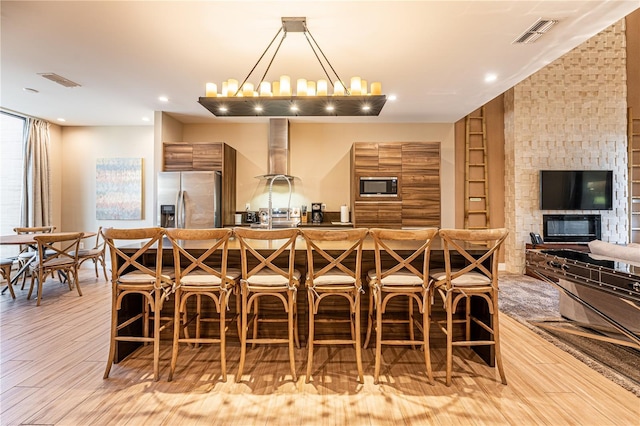 kitchen with stainless steel fridge, a breakfast bar, built in microwave, a chandelier, and light hardwood / wood-style floors