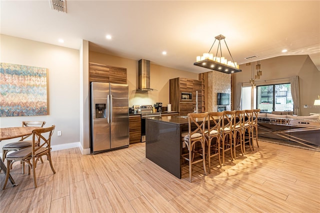 kitchen with a kitchen breakfast bar, decorative light fixtures, stainless steel appliances, and wall chimney range hood