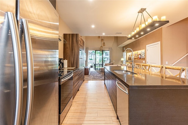 kitchen with pendant lighting, sink, stainless steel appliances, and a large island with sink