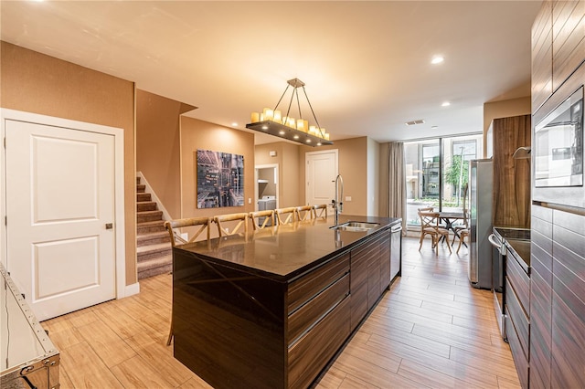 kitchen featuring light wood-type flooring, floor to ceiling windows, stainless steel appliances, sink, and a center island with sink