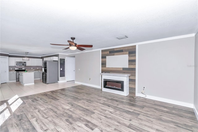 unfurnished living room with ceiling fan, a textured ceiling, light hardwood / wood-style flooring, and crown molding