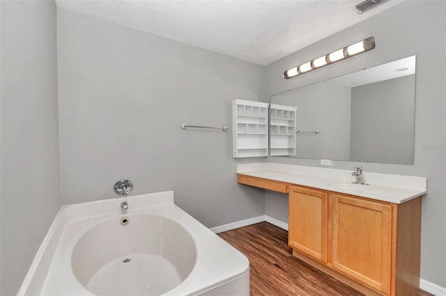 bathroom with wood-type flooring, a textured ceiling, a tub to relax in, and vanity