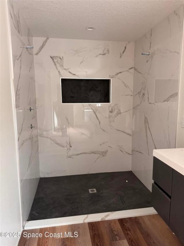 bathroom with a textured ceiling, vanity, wood-type flooring, and tiled shower