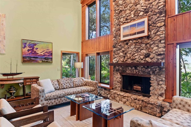 carpeted living room featuring a high ceiling, a stone fireplace, and wooden walls