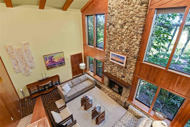 living room with a healthy amount of sunlight, beam ceiling, a fireplace, a high ceiling, and wood walls