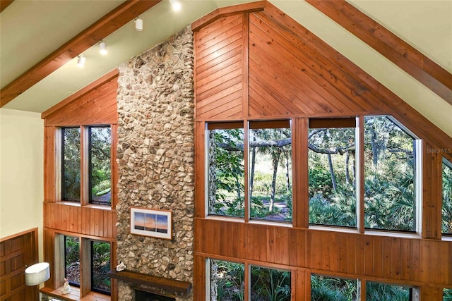 unfurnished sunroom with vaulted ceiling with beams, a stone fireplace, and a wealth of natural light