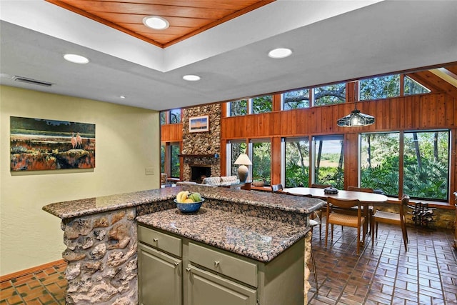 kitchen featuring a stone fireplace, light stone counters, a center island, and wooden ceiling