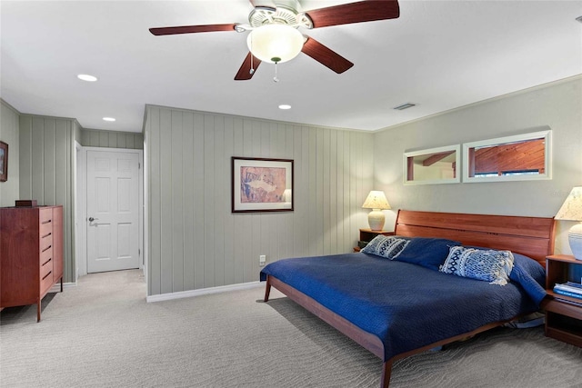 bedroom with ceiling fan, wooden walls, and light colored carpet